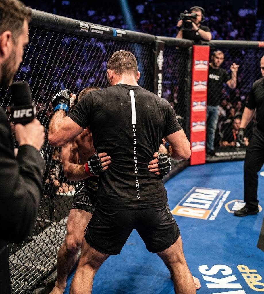 Two fighters in a cage fight scenario with a referee and camera in the background, featuring UFC branding.